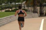 A pretty brunette with remarkable muscle definition jogs away from the camera on the deck of a marina.  Camera zooms in to follow.