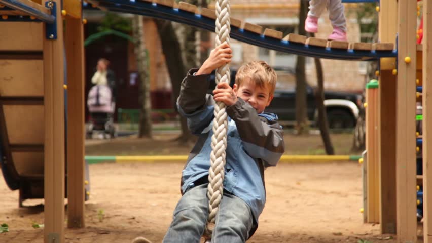 Boy sway on rope at playground at sunny autumn day