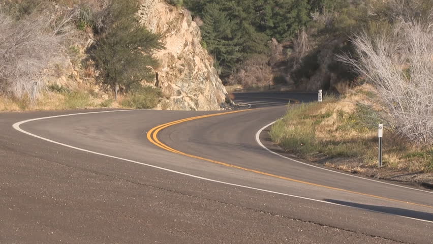 Modern grey car accelerates off of shoulder onto scenic mountain road (HD with audio).