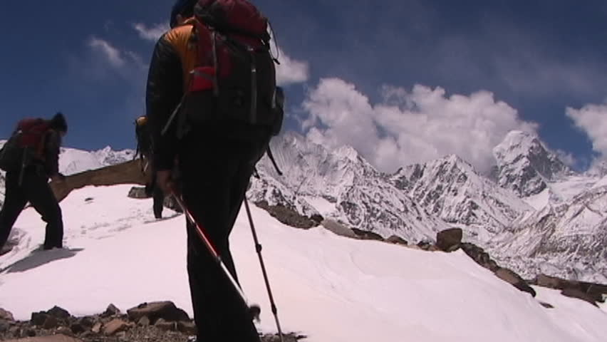 Climbers near Mt. Everest in Tibet walking over a snow hill with Mt. Pumori in the background