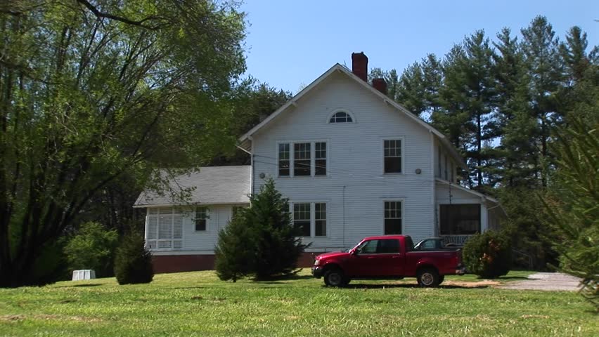 A newer model red pickup sits parked in front of a quaint white farmhouse.