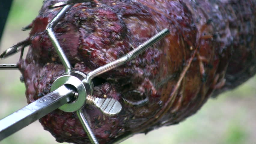 detail of savory meat roasting on a spinning rotisserie with smoke, dripping juices, and flame reflections