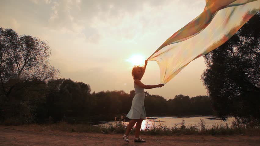 woman near to lake walks holds long silk shawl fluttering on wind