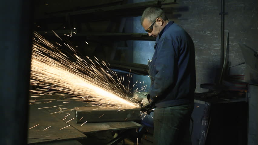 Manual worker in steel factory using circular blade on a piece of metal. Dolly shot
