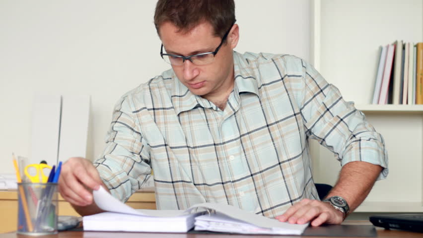 Male engineer reading documents and working on laptop