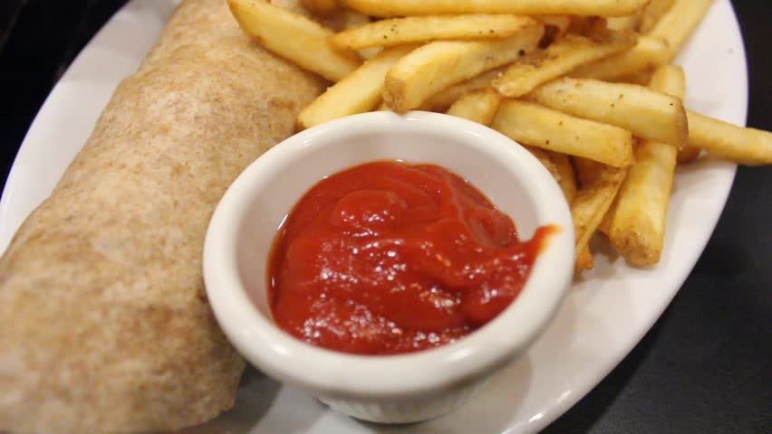 French Fries Dipped In Small Ketchup Bowl On A Plate Beside A Fresh Calzone