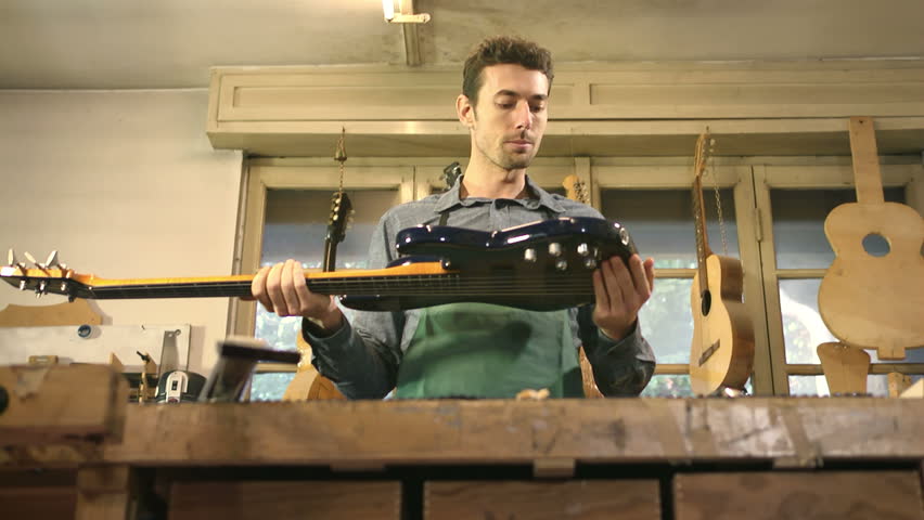 Adult man at work as artisan in italian workshop with bass guitar and musical instruments