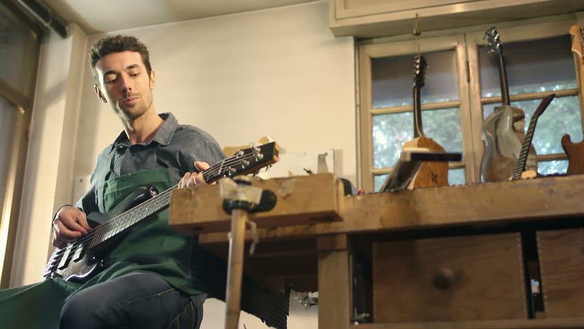 Man at work as craftsman in italian workshop playing and testing new bass guitar and musical instrument 