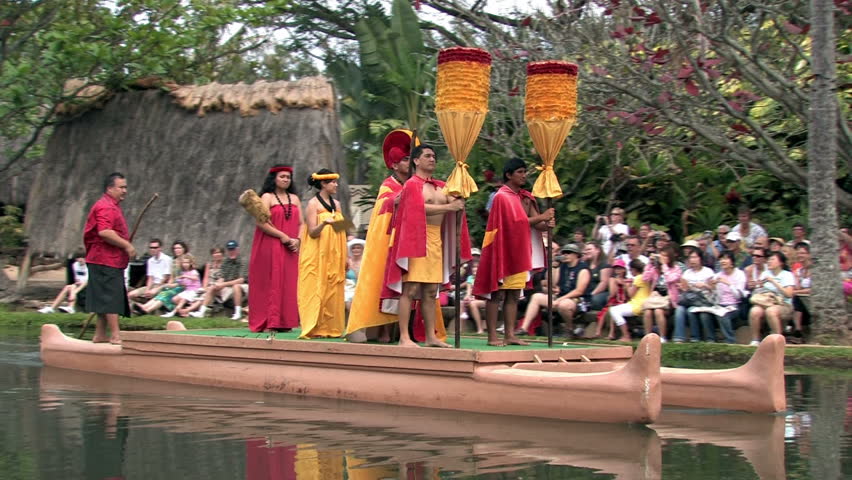 Polynesian Cultural Center in Laie Oahu Hawaii. Canoe show with dancers. Demonstration for tourists in main lagoon. Orange and red skirts on Royalty. Water, lagoon and palm trees.