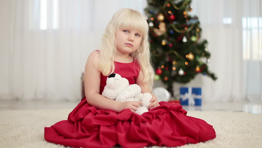 Happy child holding a teddy bear beside the Christmas tree and sits on the floor 