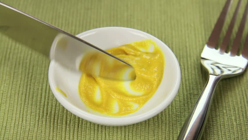 Mustard being spread on to slices of spam with an egg salad. 