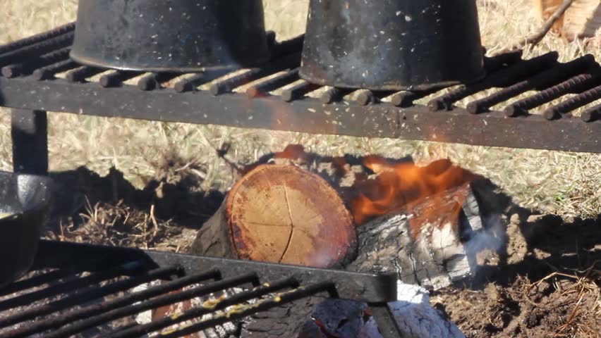Closeup of campfire under cast iron rack and two kettles