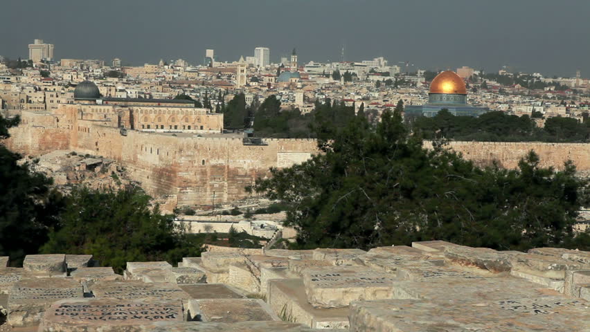 Wide slider dolly across the  graves at the Jewish cemetery of Jerusalem, Israel with the east wall of the Old City and the Temple Mount with the Dome Of The Rock and Al-Aqsa Mosque in the background.