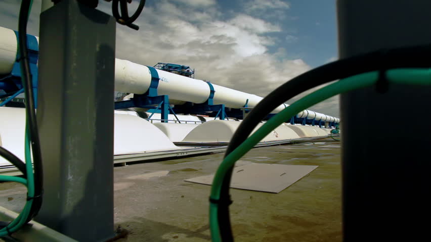 Dolly slider move up past valves and gauges on the roof of the IDE Ashkelon desalination plant in Israel, revealing the large pipes behind. Nice blue sky with fluffy clouds.