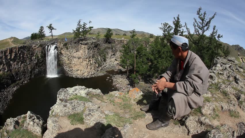 GOBI DESERT, MONGOLIA - Mongolian man crouches atop cliff and observes waterfall on July 14, 2009 in Mongolia.
