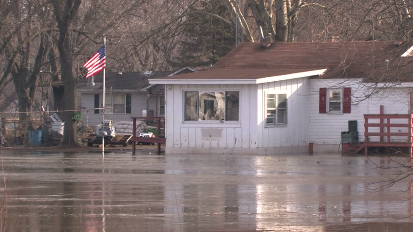 Floodwater flows around a small house with an American flag 