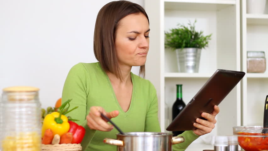Woman cooking, tasting and looking at recipe on digital tablet