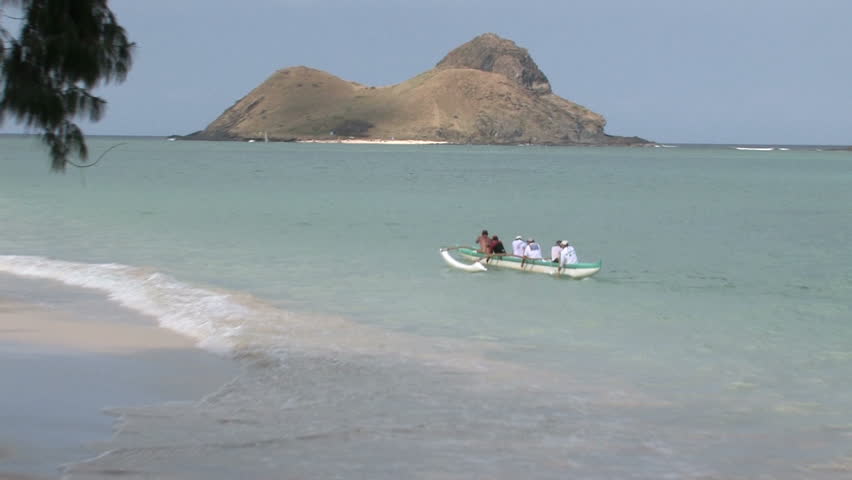 Tropical beach Oahu, Hawaii. Islands off shore in Pacific ocean. Outrigger paddling away tracking from beach to island. Waves on white sand with tree limbs overhead. Scenic, relaxing, calm seascape