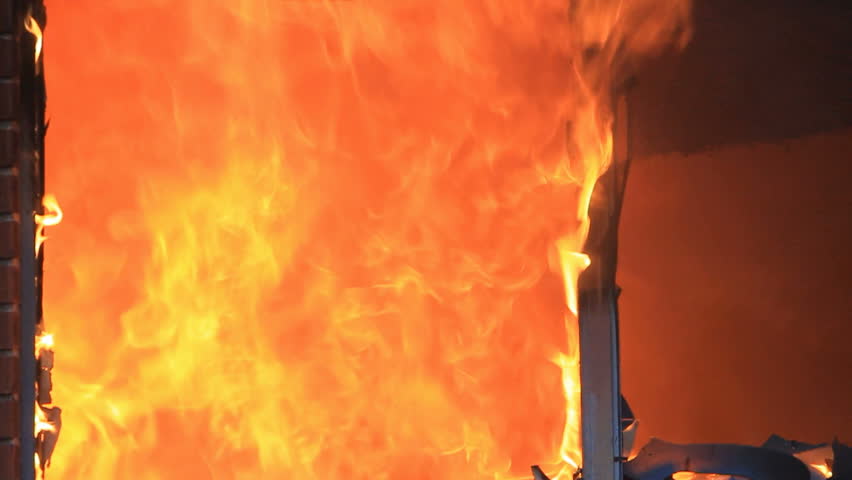 Fire burns inside window of house with explosions and intensity. Slight slow motion to emphasis the flames and sparks.