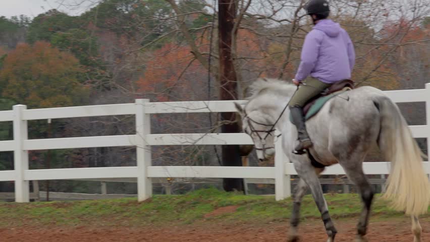 Young woman trots a white horse during practice in an outdoor arena