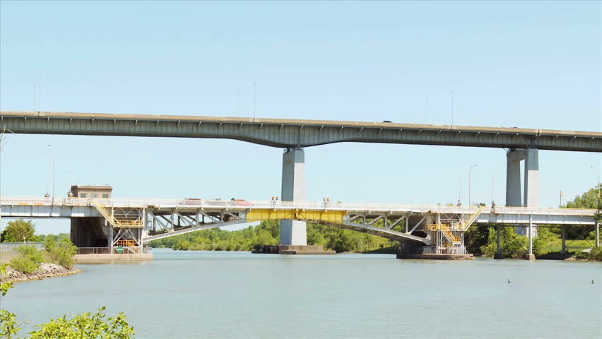 Bus driving over the Homer Lift Bridge which spans the Welland Canal, Part of Garden City Sky-way is seen in top background.