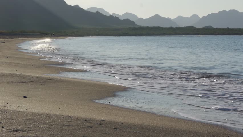 Close up of waves washing on the beach with rugged coastline