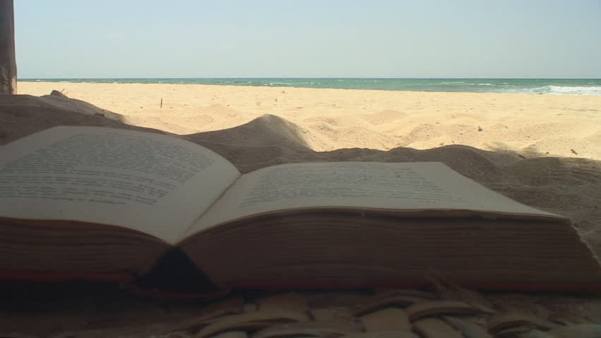 Shaded book pages flip on windy beach with sand and ocean in the background relax