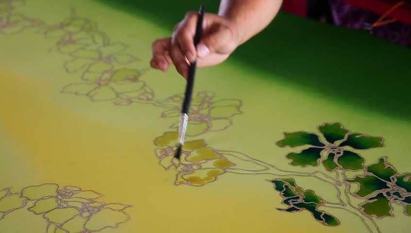 Close-up of an artist carefully paint the floral/flower motif on a yellow traditional batik fabric