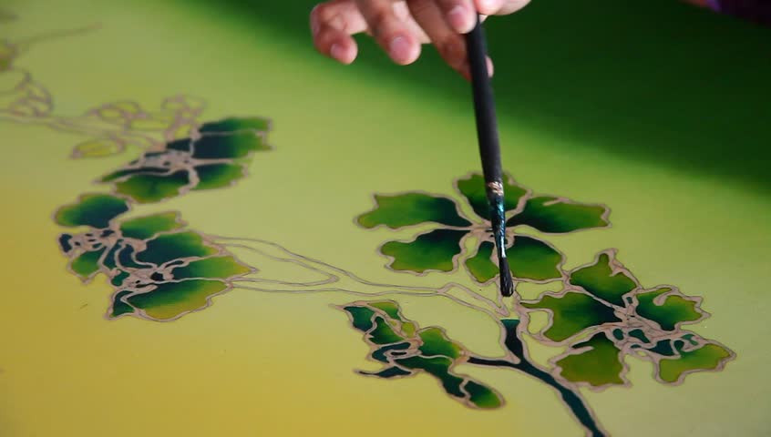 Close-up of an artist carefully touch-up the floral/flower motif on a yellow traditional batik fabric