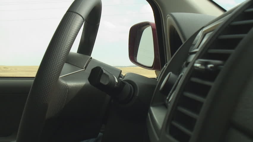Dashboard perspective of man's hand on steering wheel driving with side window background