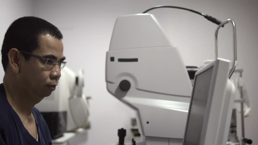 Asian doctor at work during eyesight exam and visit to adult woman in hospital room. Dolly shot