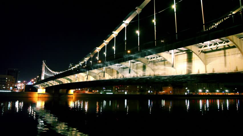Crimean bridge over river with light reflection on water, house on quay on other side at night in Moscow