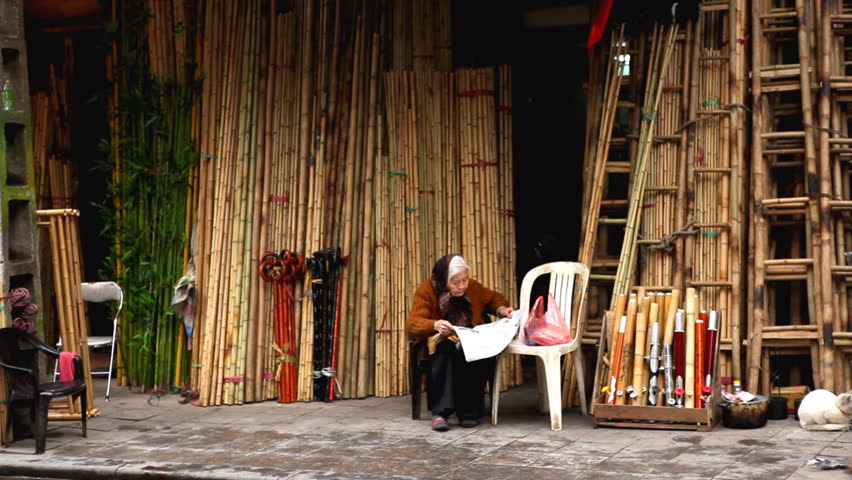 HANOI, VIETNAM - FEBRUARY 15, 2011 Old Women read newspaper and sell bamboo