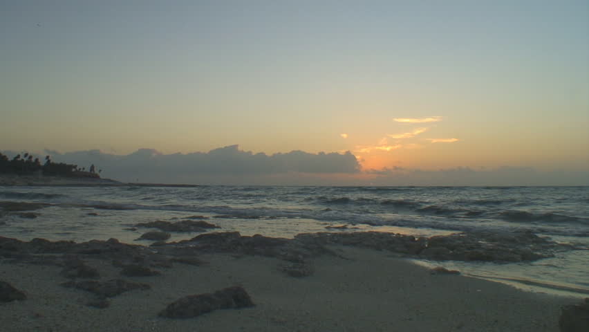 Early morning sunrise paints the horizon orange as waves meet a rocky beach