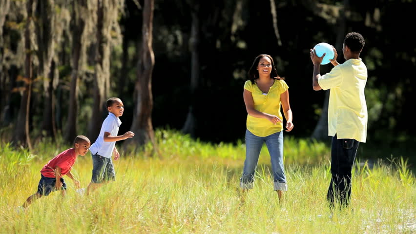 Attractive young african american family playing ball together on parkland