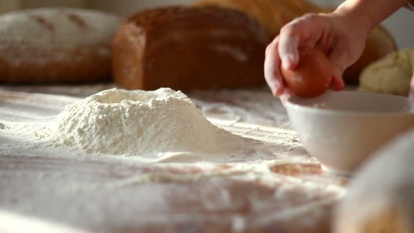 Baker adding egg to flour on table, slow motion 