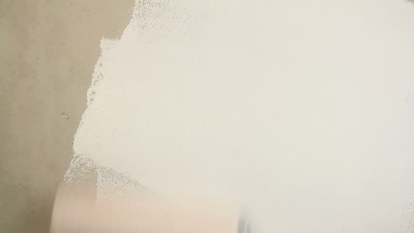Painting out a bare wall with a paint roller with white paint. 