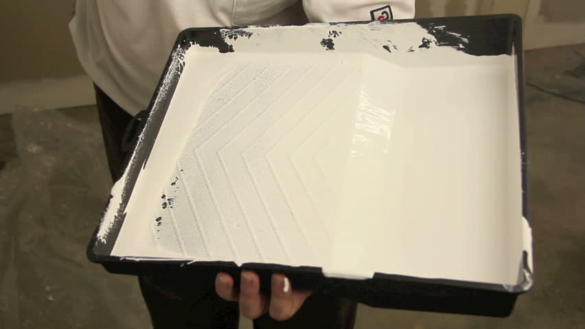 Dipping paint roller into tray and painting a wall with the roller with white paint.