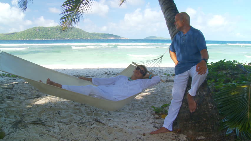 senior couple relaxing together in the shade of palmtrees on the beach