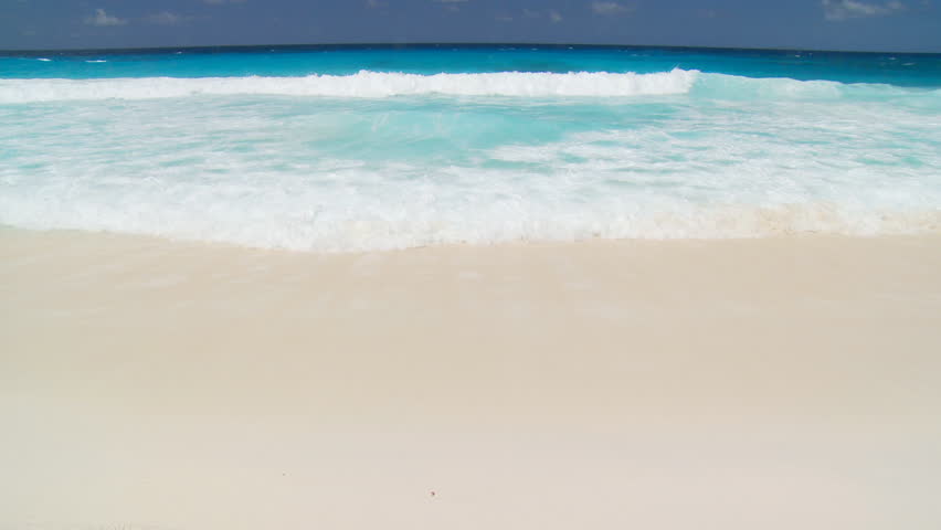 whitecaps landing on sandy beach at blue sky