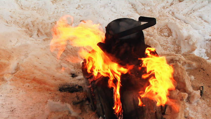 Teapot is heated on fire in wood where snow lies.