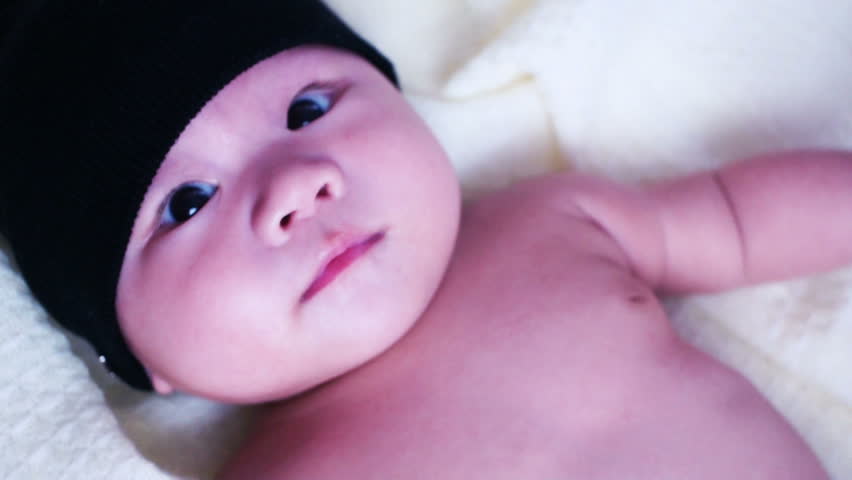 A cute little baby is looking into the camera and is wearing a black hat. 