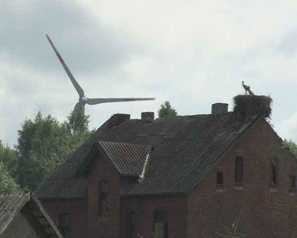 windmill spins and stork nest on abandoned rural building. Alternative wind energy generation.
