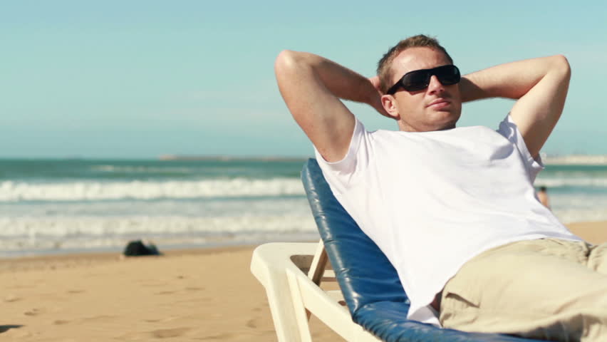 Happy young man relaxing on sunbed on the beach