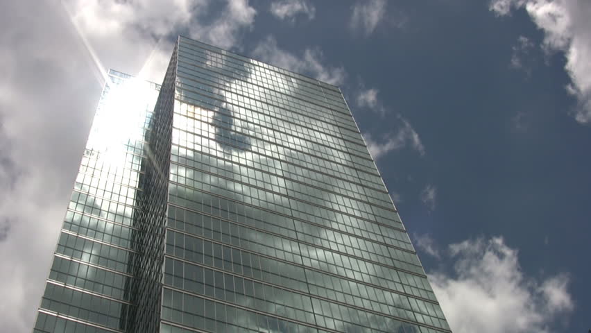 A tall mirrored skyscraper reflects the clouds going by in a timelapse shot.