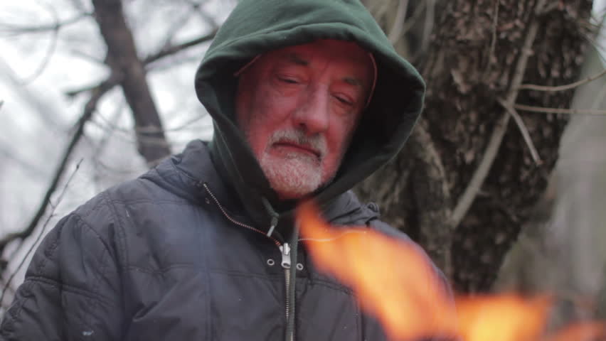 Homeless man in front of a fire, close up