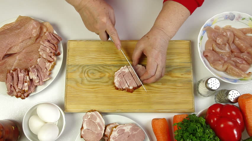 Women's hands slicing pork bacon, an ingredient for cooking chicken roll. Top view