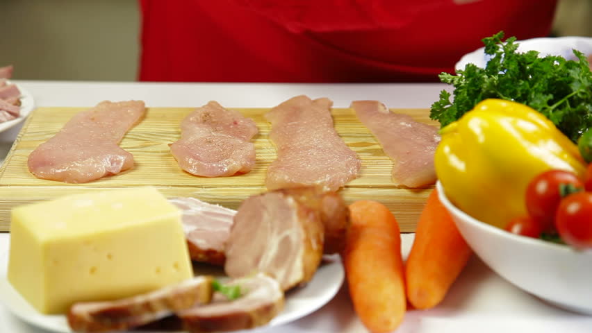 Women's hands cooking rolls of chicken breast, add salt and pepper 