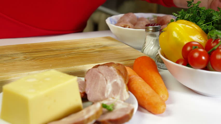 Women's hands cooking rolls of chicken breast, add bacon and cheese.