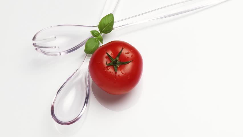 Salad servers with one tomato and basil leaves
